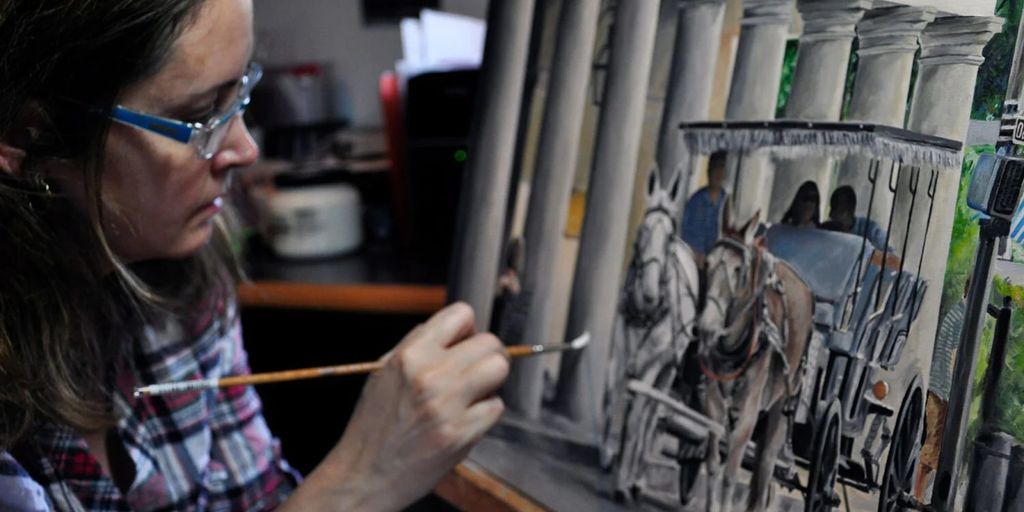 The image shows an artist painting a horse-drawn carriage with a focus on the details of the artwork being created.