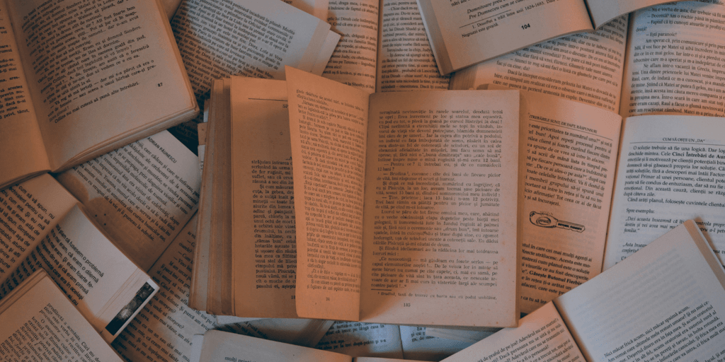 A collection of open books scattered on a surface, displaying pages with text in a warm, soft lighting.